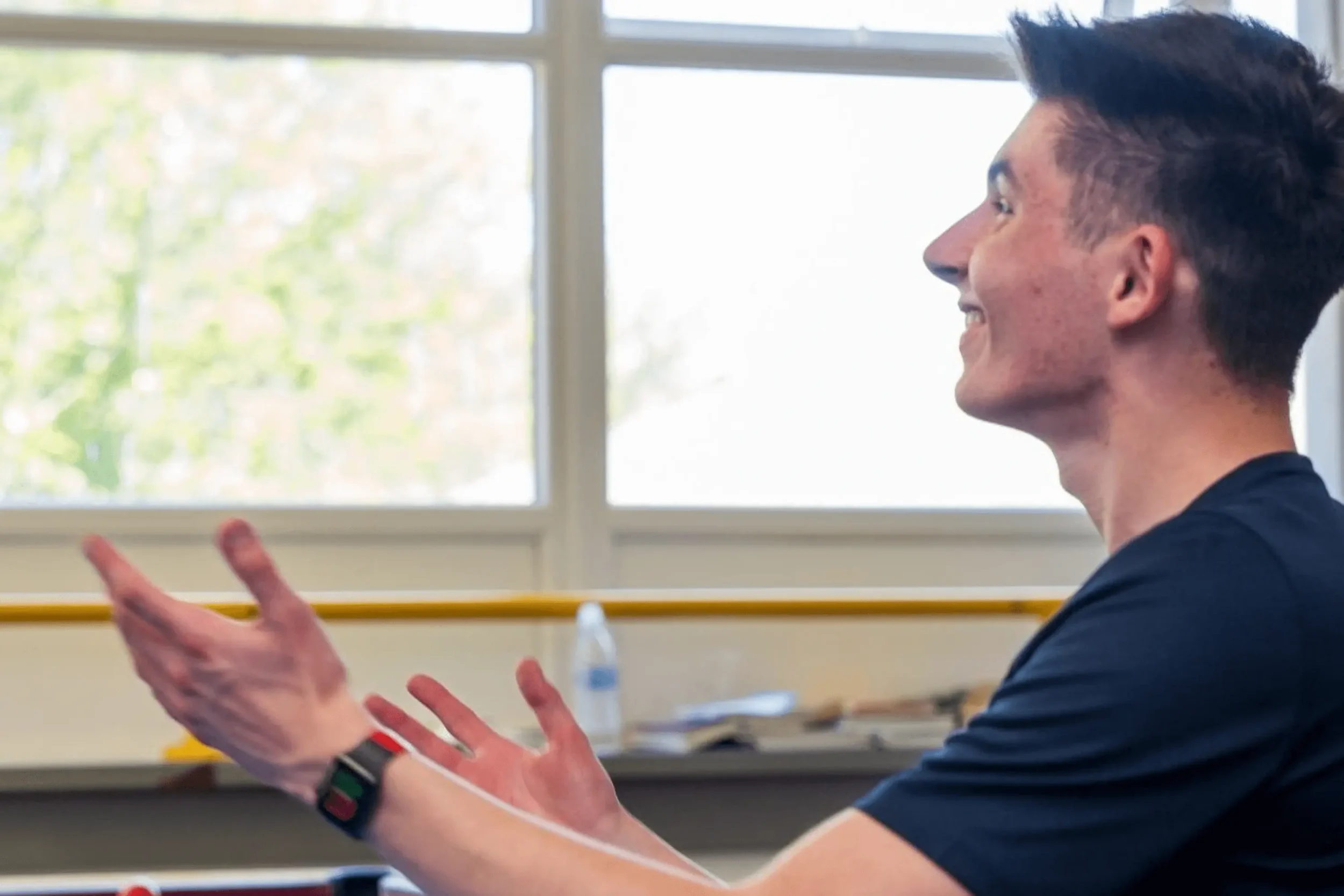 Young 18 year old white male in a navy blue tee shirt looking joyful in front of a window