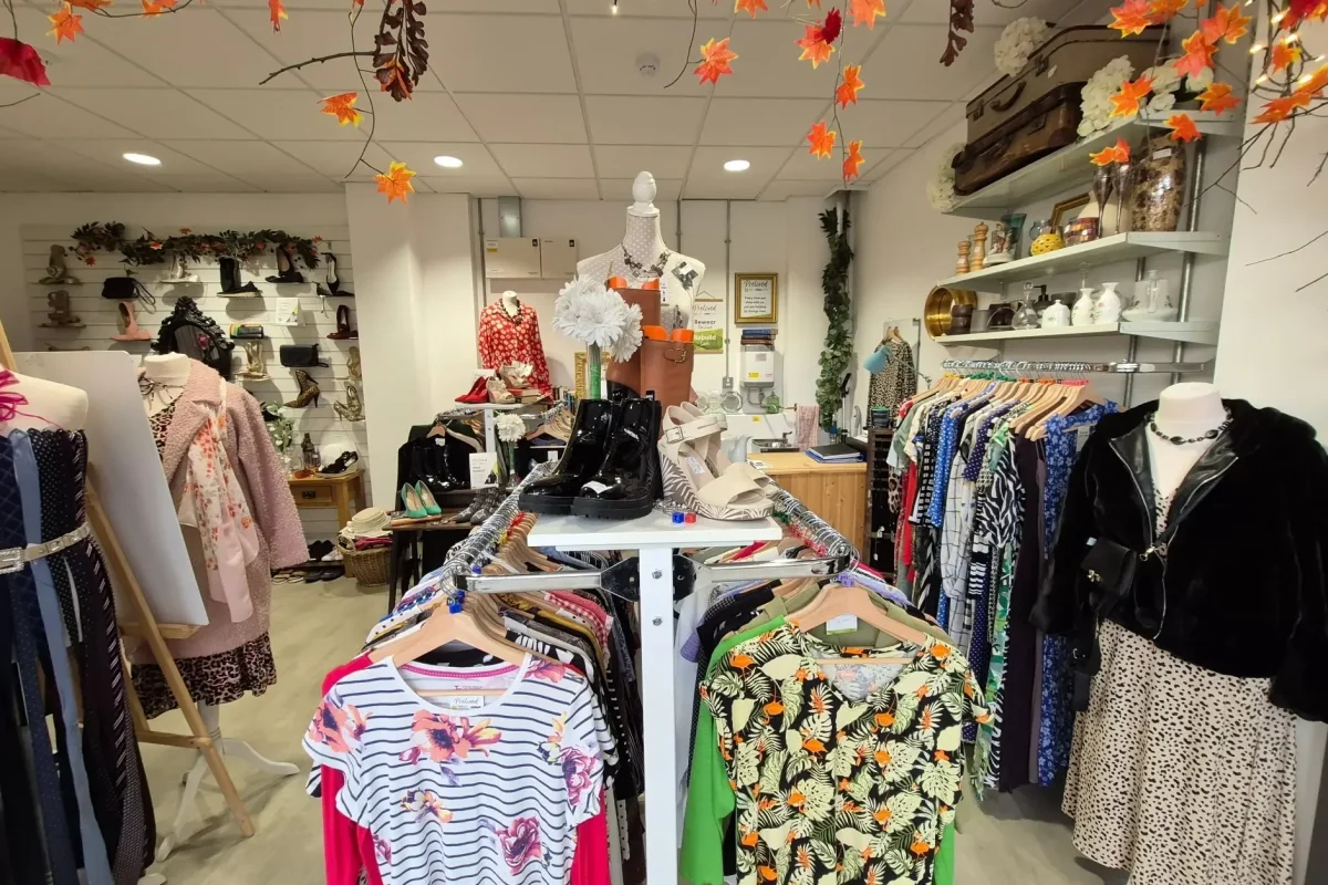 Inside of the Preloved charity shop, there are rails of clothes and shoes on the shelves.